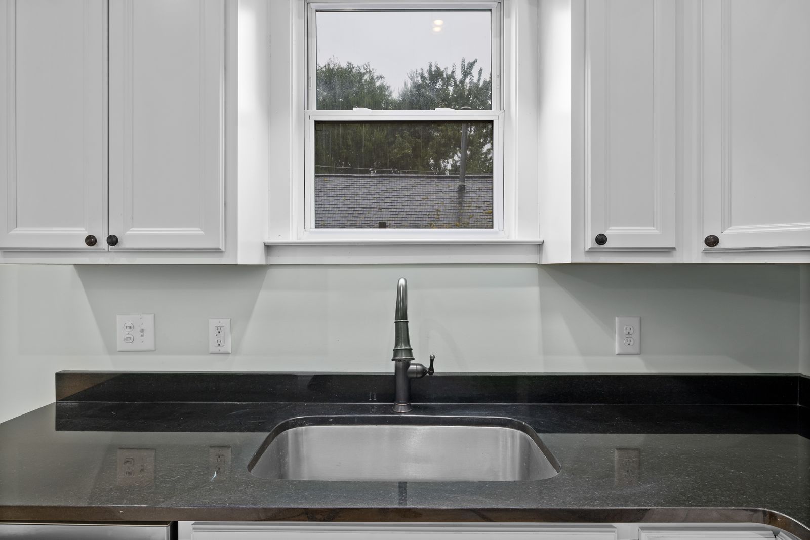 Single bowl stainless steel undermount sink set into a dark granite countertop in a Bengaluru kitchen, 2026, by myNivasa