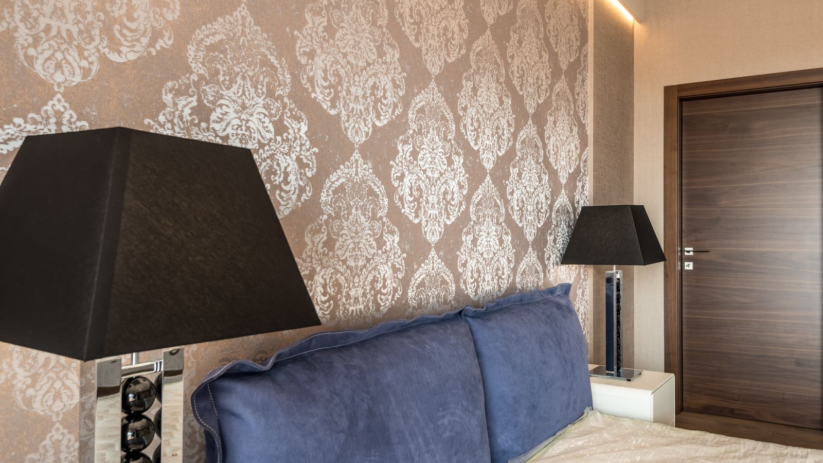 Bedroom headboard wall with a silver damask wallpaper repeat and blue cushions, Bengaluru 2026, by myNivasa