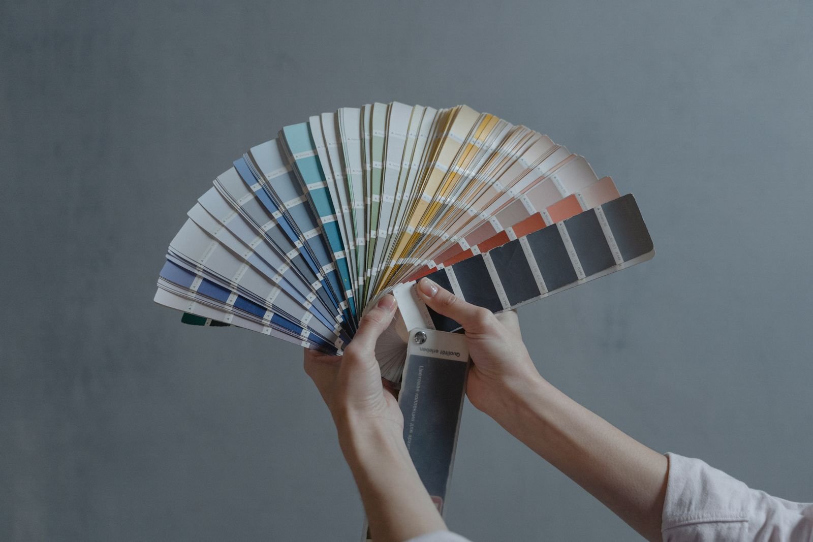 Hands holding a paint swatch fan against a grey wall while choosing wall colours, 2BHK repaint Bengaluru 2026, by myNivasa