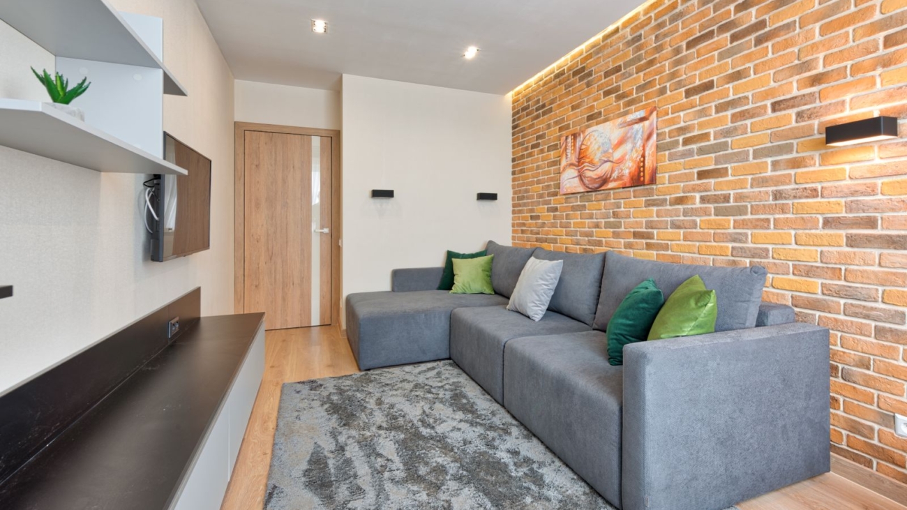 Grey L-shaped sofa with chaise facing a wall-mounted TV in a Bengaluru living room, 2026, by myNivasa