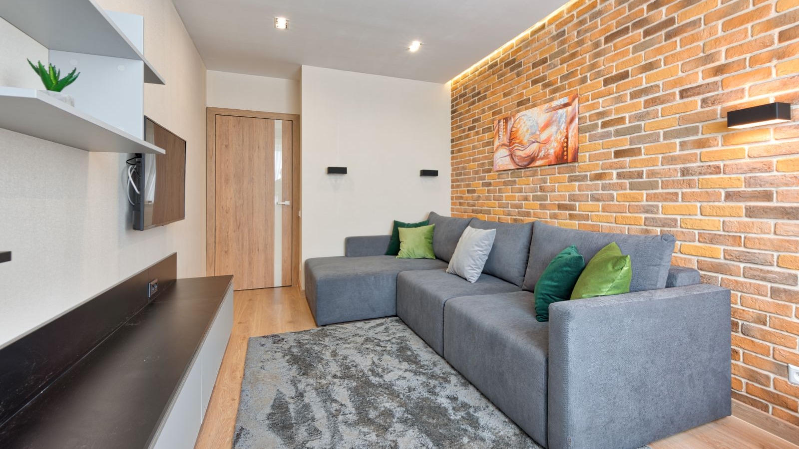 Grey L-shaped sofa with chaise facing a wall-mounted TV in a Bengaluru living room, 2026, by myNivasa