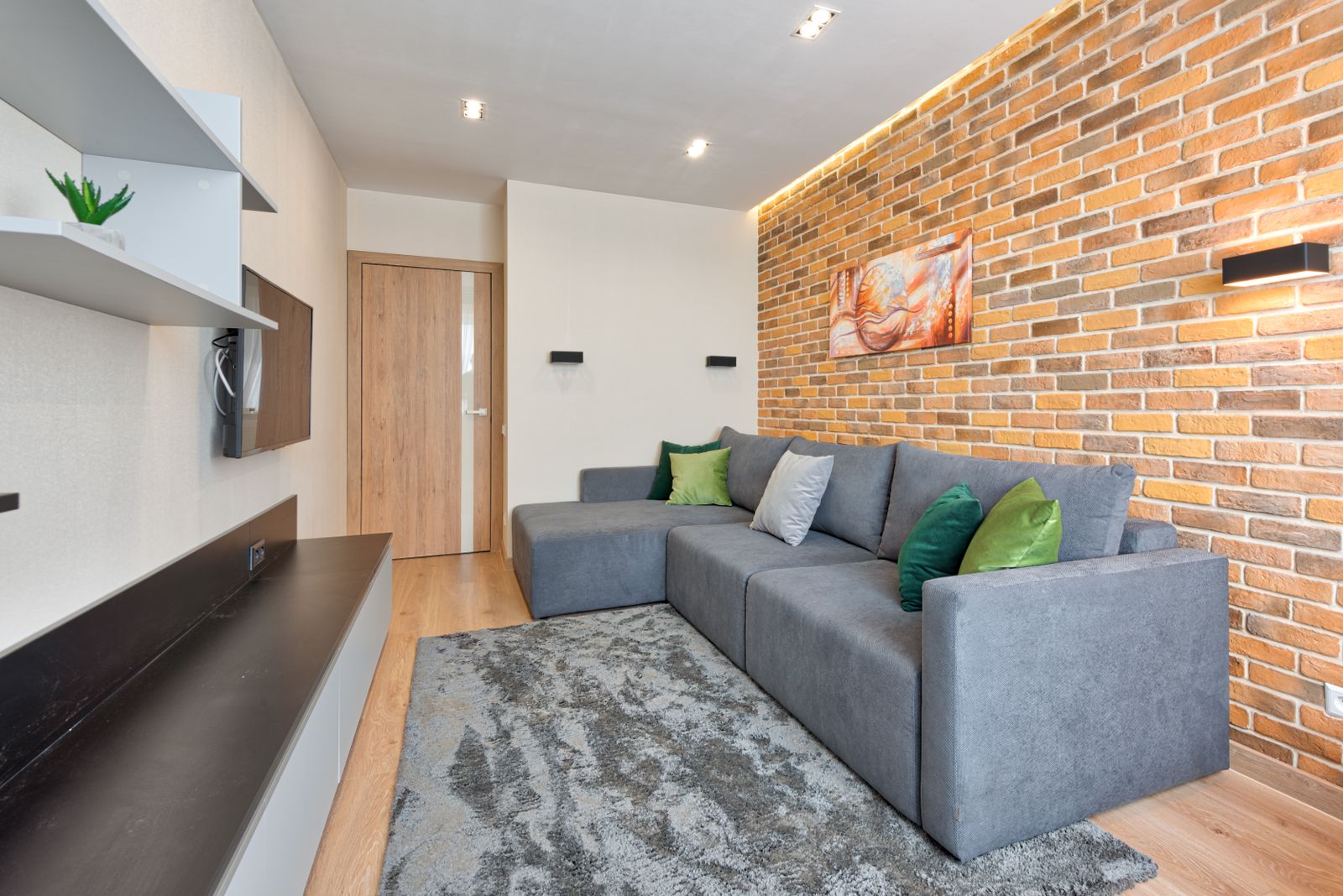 Grey L-shaped sofa with chaise facing a wall-mounted TV in a Bengaluru living room, 2026, by myNivasa