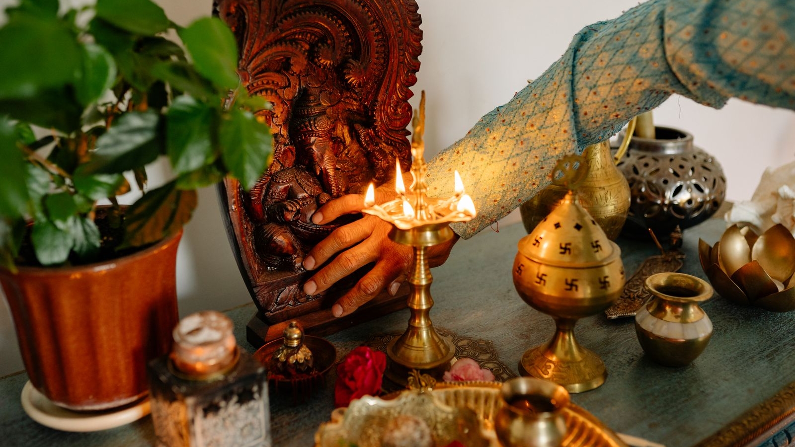 Brass lamp lit beside a carved wooden idol and plant on a home altar shelf, pooja corner guide, Bengaluru 2026, by myNivasa
