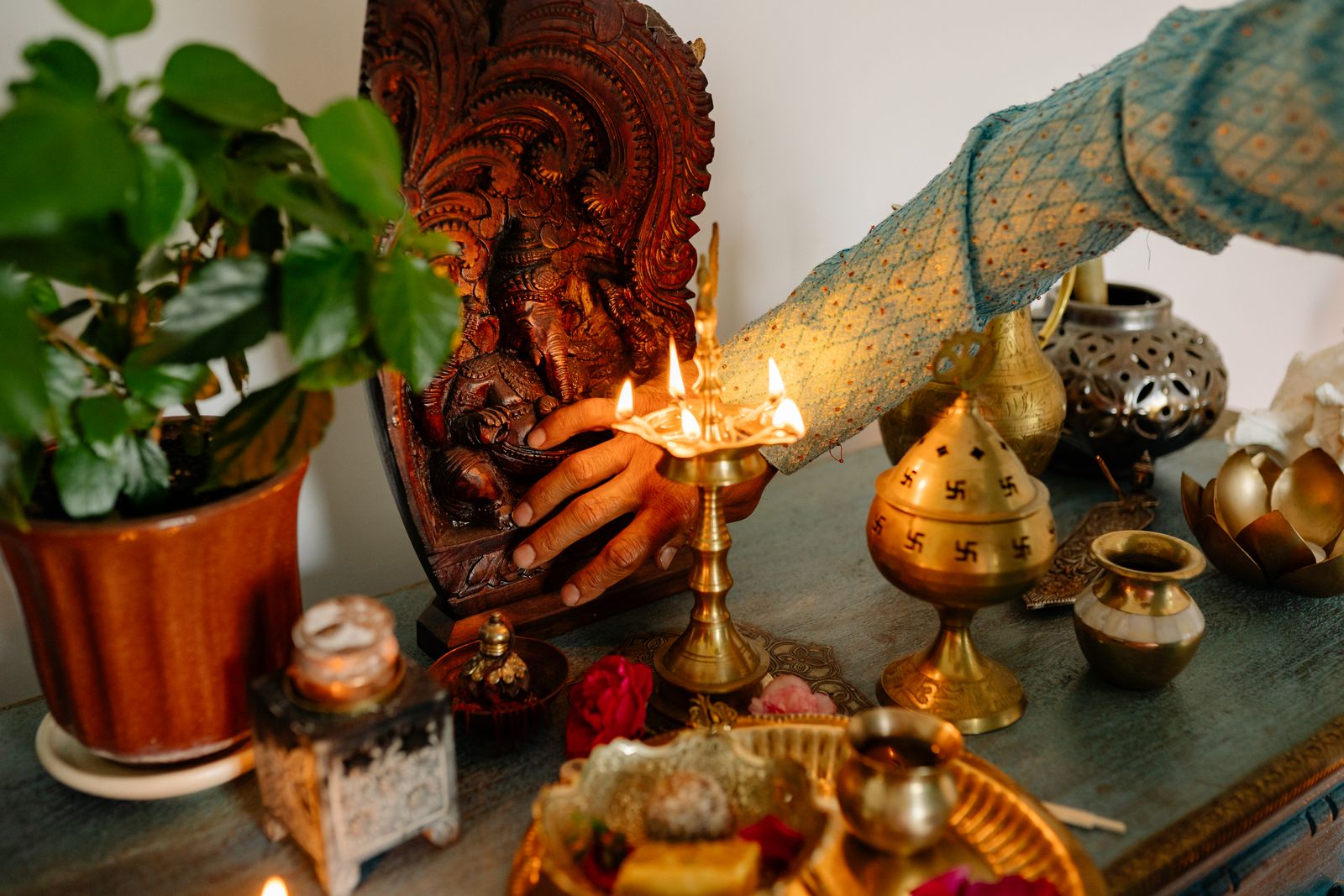 Brass lamp lit beside a carved wooden idol and plant on a home altar shelf, pooja corner guide, Bengaluru 2026, by myNivasa